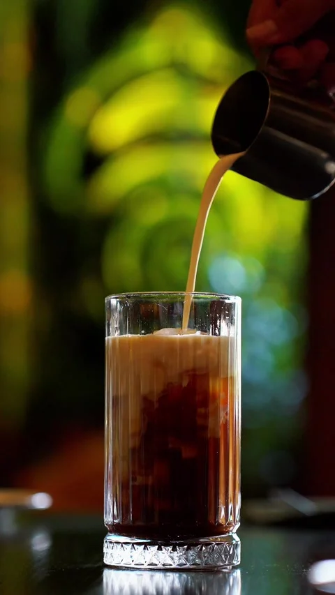 Front view of iced coffee with milk pouring into glass in cafe setting Stock Footage 329288649