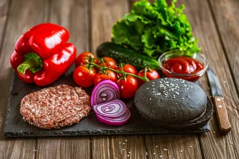 Front view of ingredients for beef black burger on a black stone board with Stock Photos