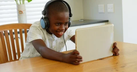 Front view of little black boy playing game on digital tablet at dining table in Stock Footage 101471721