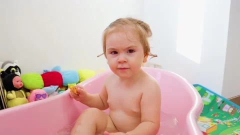 Front view looking at camera child girl sit in bath frowns smiles hold a yellow Stock Footage 208431965