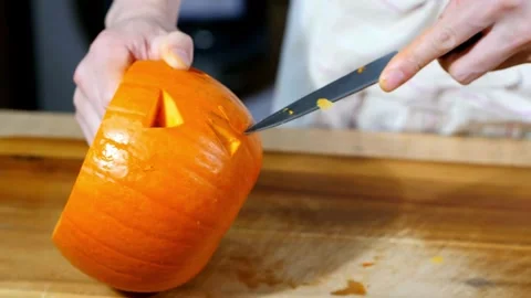 Front view of a man sitting at a table and carving an evil face into a pumpki Stock Footage 272459726