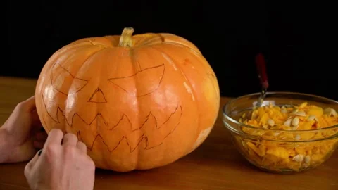 Front view of a man sitting at a table and carving an evil face into a pumpki Stock Footage 272460222
