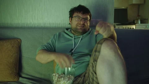 Front view of a man on a sofa watching TV and making a displeased expression Stock Footage 314519333