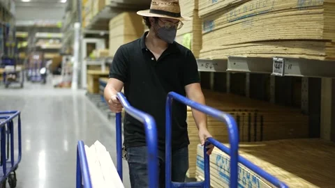 Front view of man wearing face mask moving cart in big box hardware store loaded 스톡 동영상 158379419
