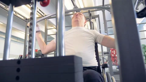 Front view of a man in a wheelchair lifting weights with an exercise machine Stock Footage 87609728