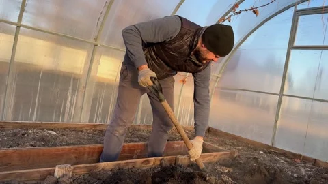 Front view of man in working gloves digging ground in wooden raised beds Stock-Footage 346035270
