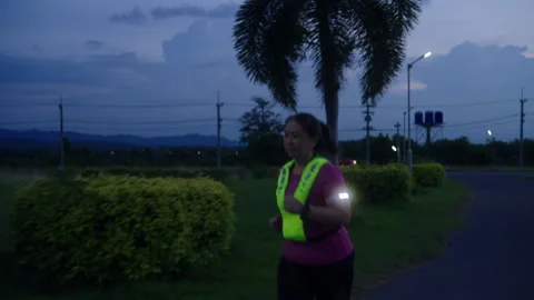 Front view of a middle-aged Asian woman jogging at twilight Stock Footage 335759569