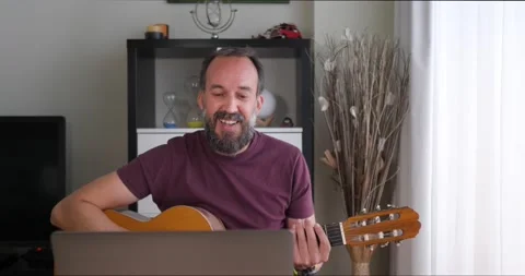 Front view of middle-aged man at home receiving guitar lessons via conference Stock Footage 154636549