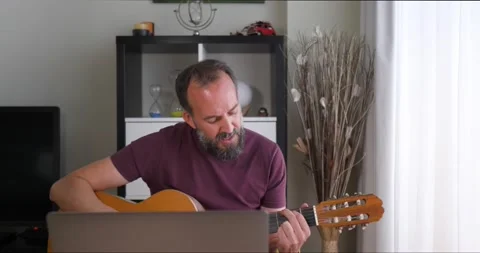 Front view of middle-aged man with beard playing guitar in front of his lapto Stock Footage 160401225