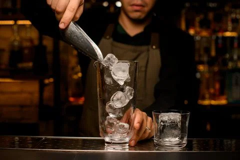 Front view of mixing cup into which the hand of male bartender pours ice cubes Foto stock