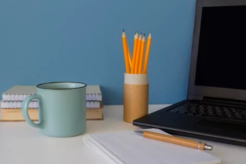 Front view on modern creative workspace. Laptop with black screen, blue cup of Stock Photos