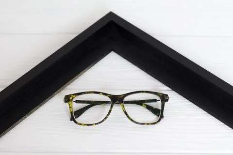 Front view of modern glasses in left corner of black frame on white wooden ba 스톡 사진