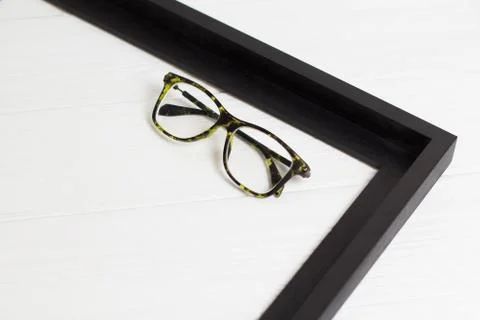 Front view of modern glasses in right corner of black frame on white wooden b Stock Photos