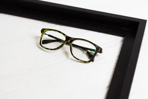 Front view of modern glasses in right corner of black frame on white wooden b Stock Photos