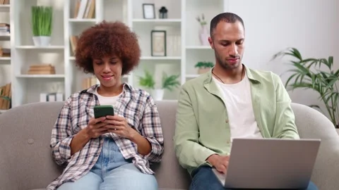 Front view of multiracial man and woman sitting on couch in living room and Video stock 251649389