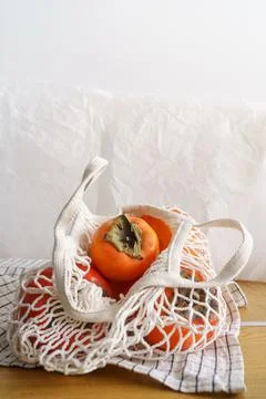 Front view orange persimmon in string bag natural light Stock Photos