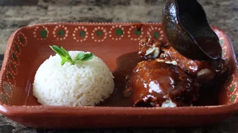 Front view of person pouring mole sauce and sesame seeds on chicken pieces .. Stock Footage 275843355