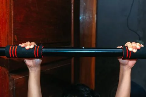 A front view of a person's hands gripping a black pull-up bar mounted on a .. Stock Photos