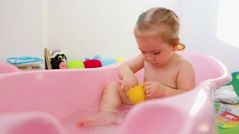 Front view playing happy little girl bathing in baby bath attentively playing Stock Footage 208435927