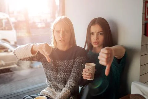 Front view portrait of two funny friends with thumbs down and looking to the  库存照片