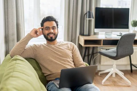 Front view of positive Hindi man in smart casual clothes using laptop while Stock Photos