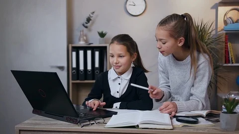 Front view of pretty serious 15-aged girl which helping her younger sister to do Stock Footage 124698792