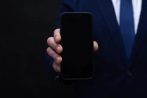 Front view of a professional man in a navy suit showing a mockup cellphone wi Stock Photos