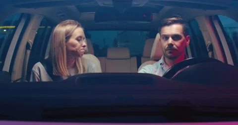 Front view of the serious couple driving on night road into the city while man Stock Footage 157360466