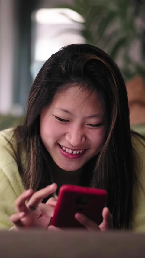 Front view smiling Asian attractive woman using cell phone lying on sofa in Stock Footage 275165599