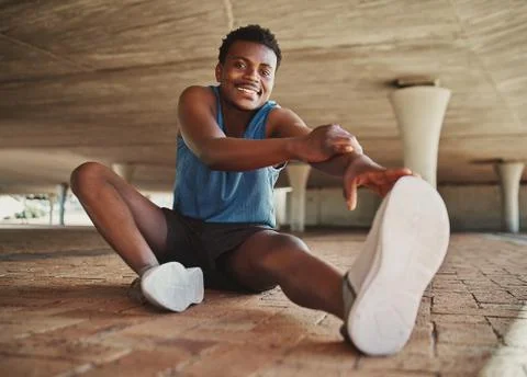Front view of a smiling fit young man wearing sneakers stretching his leg before Stock Photos