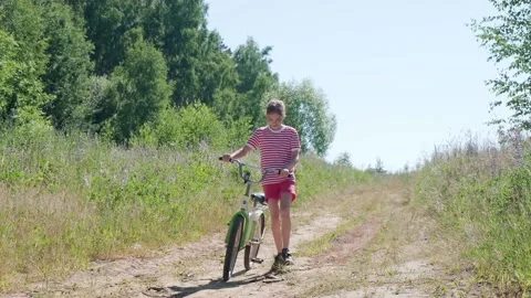 Front view of a smiling girl 9-10 years old walking next to a bicycle on a rural Stock Footage 202057582