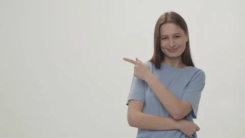 Front view of smiling girl pointing with finger to the side. Brunette young 库存影片 232884145