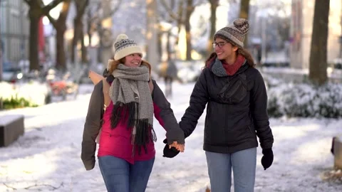 Front view of smiling young couple holding hands and walking down a snowy street Stock Footage 258370969