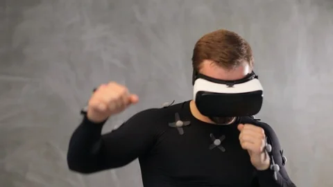 Front view of sport athletic man in VR glasses and mocap suit fighting on grey Stock Footage 93526708