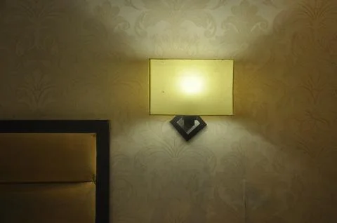 Front view of square shape wall light lamp near to bed  Stock Photos