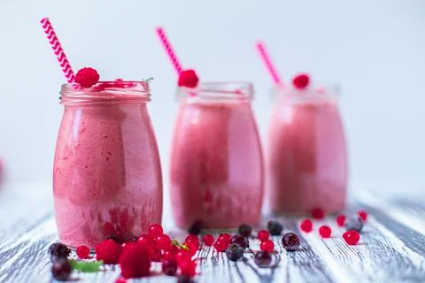 Front view of three berries milkshakes in glasses jars with ingredients on Stock Photos