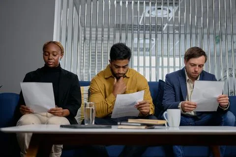 Front view of three multiracial young adults in businesswear sitting on sofa and Stock Photos