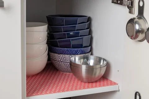 Front view of a tidy kitchen cabinet lined with a red mat, holding stacked .. Stock Photos
