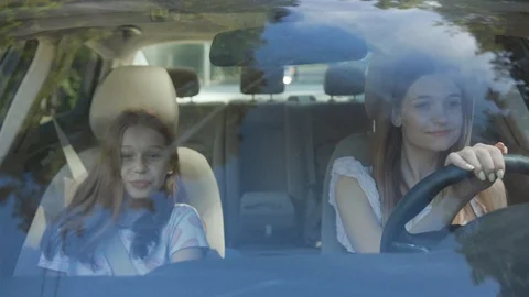 Front view two attractive girls driving a car through city on sunny day. Two Stock Footage 112748928
