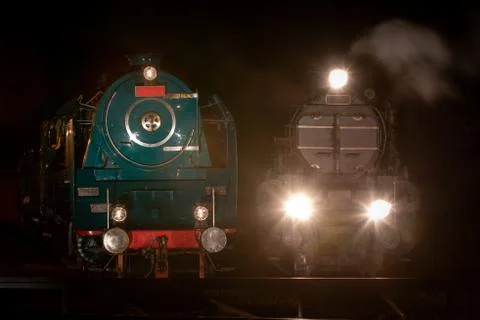 Front view of two historic steam locomotives at depot illuminated at night Stock Photos