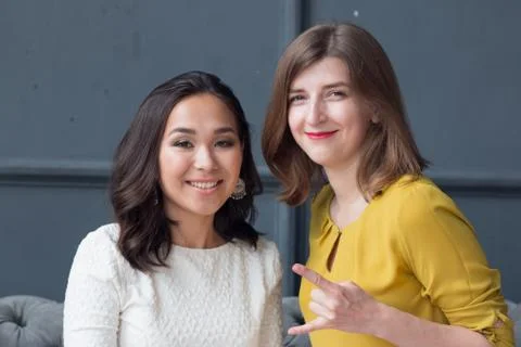 Front view of two smiling young female friends sitting in the living room at Stock Photos