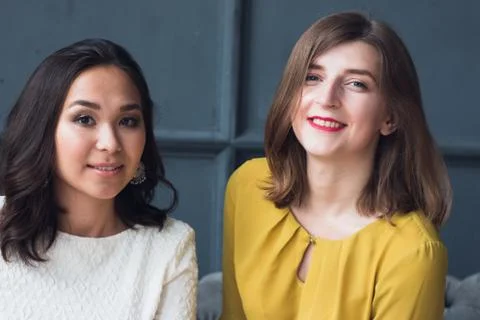 Front view of two smiling young female friends sitting in the living room at Stock Photos