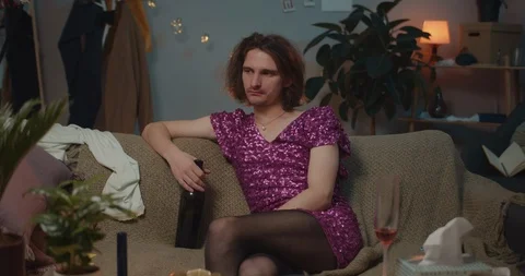 Front view of unhappy drunk transgender man sitting on sofa near smartphone and Stock Footage 125630758