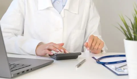 Front view at unrecognizable doctor using calculator with laptop and stethosc Stock Photos
