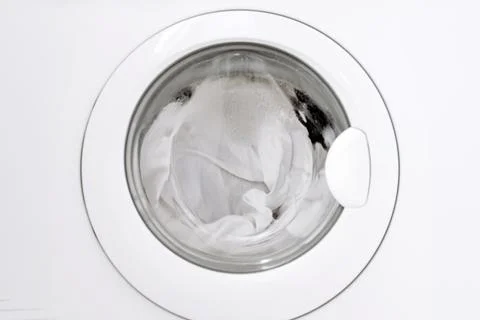Front view of a washing machine door with white laundry spinning inside, sh.. Stock Photos