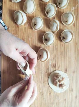 Front view of woman's hands making meat dumpling with wooden rolling pin. Stock-Fotos