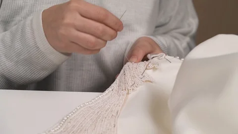 A front view of woman's hands stitching beaded lace down the wedding dress Video stock 99047641