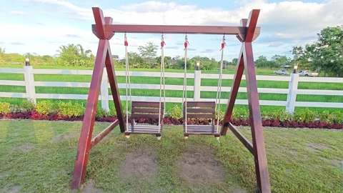 Front view of a wooden swing set next to a white fence and green rice field. Stock Footage 347457769