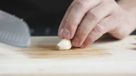 Front view of yong man cook cut thin slices of garlic with knife on cutting Stock Footage