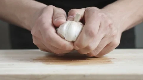 Front view of yong man cook cleans a head of garlic from the husk cutting Board Stock Footage 74345982